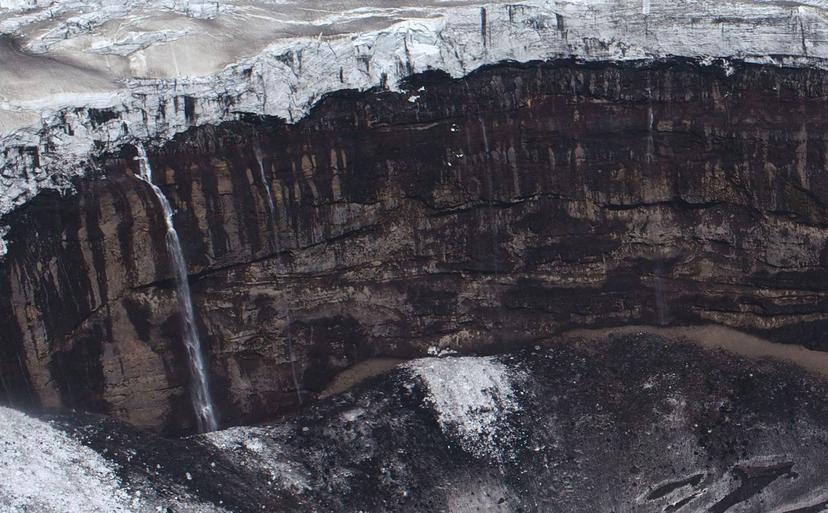 Jagged ice formations rest on a cliff top, contrasting with dark basalt rock along the cliff face below.
