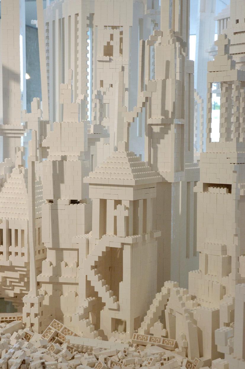 A dense cluster of white plastic building-brick structures, showing stacked blocks, tall column-like forms, stepped roofs and narrow staircases. Loose bricks are piled at the base, and the tightly packed towers fill the frame.