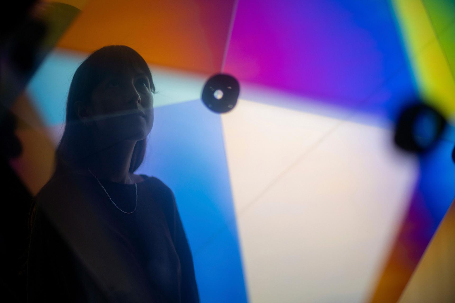 A person is seen through a glowing geometric form whose translucent panels show gradients of blue, purple, orange and yellow around dark circular connectors.