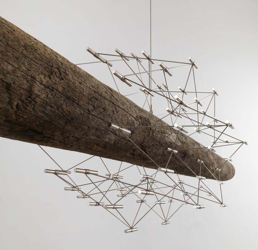Thin rods form a delicate network of triangular shapes that extend outwards from the log’s surface, with cylindrical metal connectors connecting the geometric lattice.