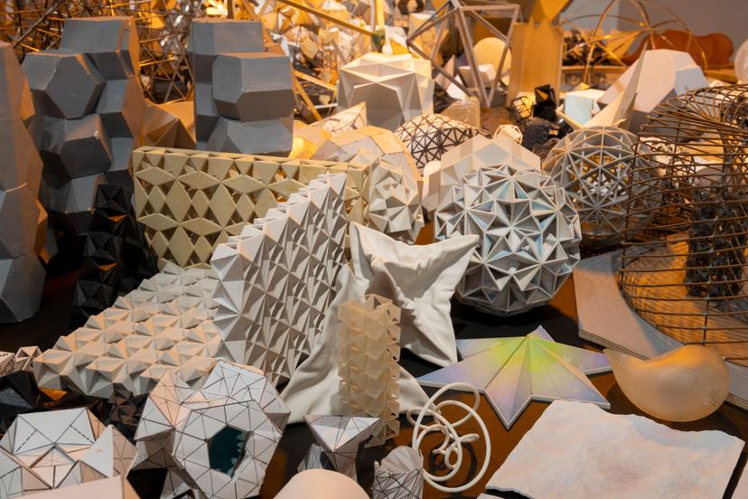 A close-up view of a dense cluster of geometric models, including faceted spheres, folded panels, latticed forms and star-shaped pieces.